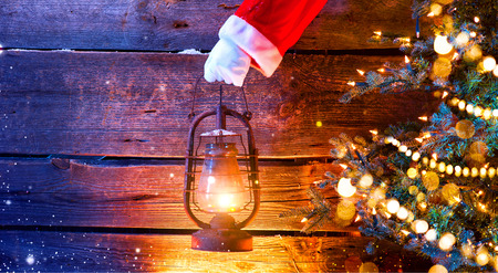 Christmas scene. Santa's hand holding vintage oil lamp over wooden backgroundの写真素材