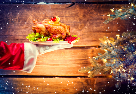 Christmas holiday dinner. Santa's hand holding roasted chicken over wooden backgroundの写真素材