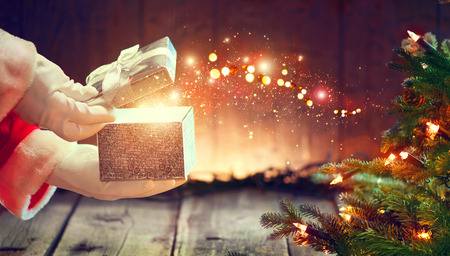 Santa Claus opens gift box over wooden background with Christmas treeの写真素材