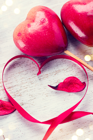 Valentine's Day. Elegant red satin gift ribbon and couple of red hearts over white wooden backgroundの写真素材