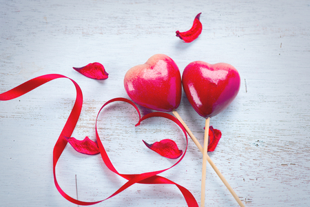 Valentine's Day. Elegant red satin gift ribbon and couple of red hearts over white wooden backgroundの写真素材
