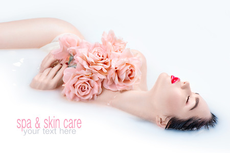 Beautiful Fashion model girl with bright makeup and pink roses taking milk bath, spa and skin care conceptの写真素材
