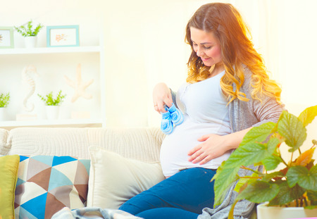 Pregnant happy woman holding blue baby shoes in her handsの写真素材