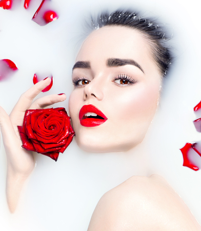 Beauty young model girl with bright makeup and red rose flower relaxing in milk bathの写真素材
