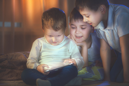 Three little boys with tablet computer in a dark room. Kids playing games on tablet pcの写真素材