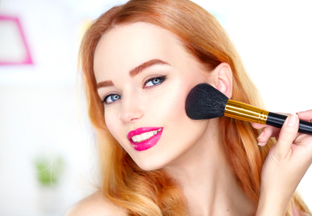 Beauty woman applying makeup. Beautiful girl looking in the mirror and applying cosmetic with a big brushの写真素材