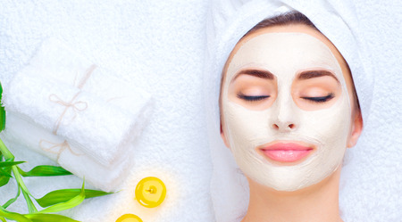 Spa woman applying facial mask. Closeup portrait of beautiful girl with a towel on her head applying facial clay maskの写真素材