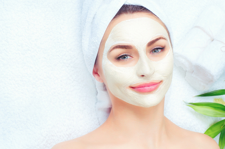 Spa woman applying facial mask. Closeup portrait of beautiful girl with a towel on her head applying facial clay maskの写真素材