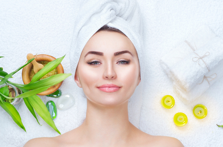 Spa woman applying facial mask. Closeup portrait of beautiful girl with a towel on her head applying facial clay maskの写真素材