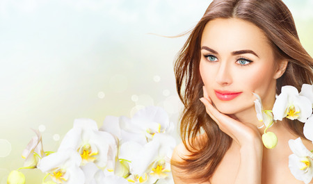 Beauty woman with orchid flowers. Beautiful spa girl touching her faceの写真素材