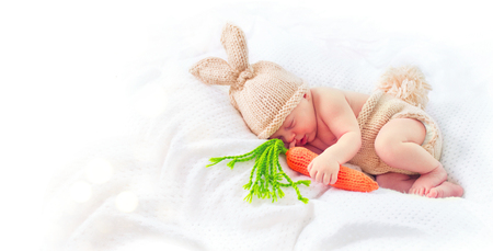 Cute two weeks old smiling newborn baby boy wearing knitted bunny costume, hat with rabbit ears, tail and funny carrot toy. Sweet baby portraitの写真素材