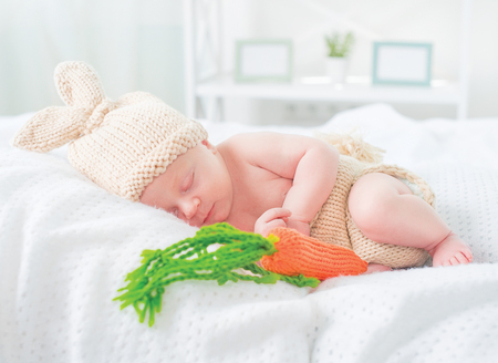 Cute two weeks old smiling newborn baby boy wearing knitted bunny costume, hat with rabbit ears, tail and funny carrot toy. Sweet baby portraitの写真素材