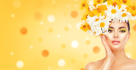 Beauty girl with daisy flowers hairstyle touching her skin. Model woman with blooming chamomile flowersの写真素材