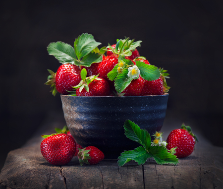 Strawberries in a bowl with leaf and blooming flower close-up over wooden backgroundの写真素材