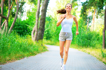 Beauty young woman with earphones running in the park. Full length portraitの写真素材