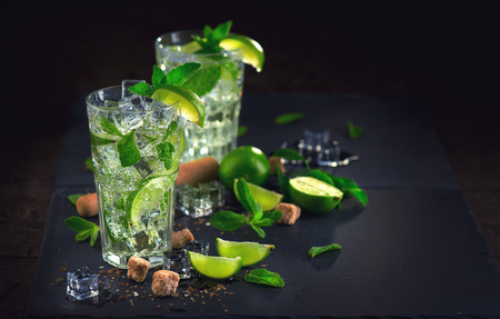 Mojito cocktail on a table. Summer cocktail with rum, lime, mint, ice cubes and brown sugarの写真素材