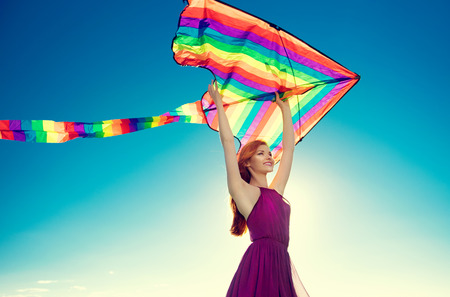 Beauty redhead girl with flying colorful kite over clear blue skyの写真素材