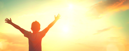 Little boy raising hands over sunset sky, enjoying life and natureの写真素材