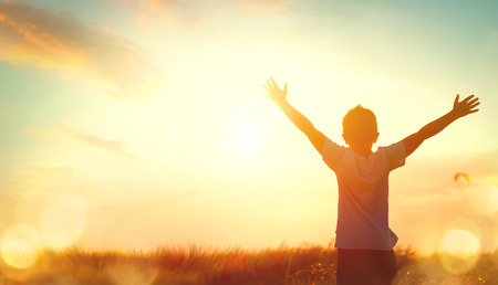 Little boy raising hands over sunset sky, enjoying life and natureの写真素材