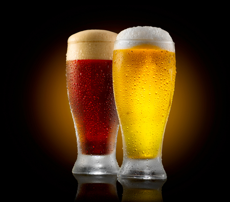 Craft beer. Two glasses of cold light and dark beer isolated on black backgroundの写真素材