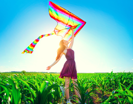 Beauty redhead girl with flying colorful kite over clear blue skyの写真素材