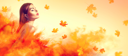 Beautiful fashion woman in autumn yellow dress with falling leaves posing in studioの写真素材