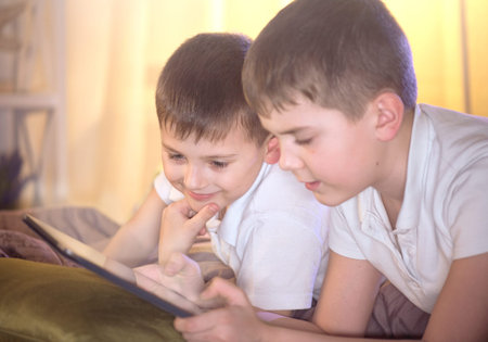 Two kids using tablet pc in bedroom. Little boys watching movie together
