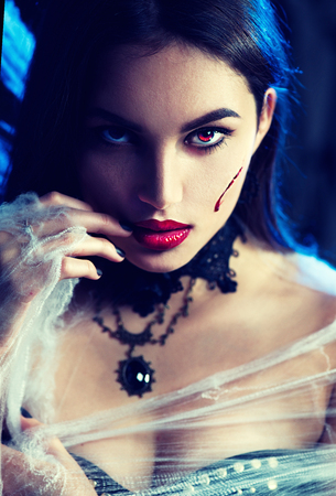 Halloween. Beauty sexy vampire woman posing in darkness, wearing spider webの写真素材