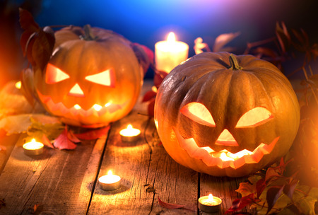 Halloween pumpkin head jack lantern with burning candles over wooden backgroundの写真素材