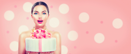 Fashion model girl holding beautiful party or birthday cake isolated on pink background. Wide angleの写真素材