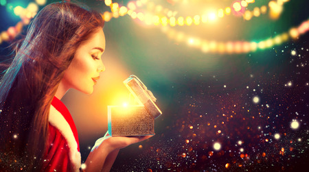 Christmas scene. Beauty brunette young woman in party costume opening gift box over holiday blurred backgroundの写真素材