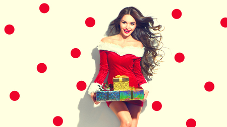 Christmas scene. Sexy Santa. Beauty model girl wearing red party costume holding giftsの写真素材