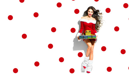 Christmas scene. Sexy Santa. Beauty model girl wearing red party costume holding giftsの写真素材