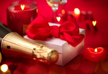 Valentine's Day romantic dinner. Date. Champagne, candles and gift box over holiday red backgroundの写真素材