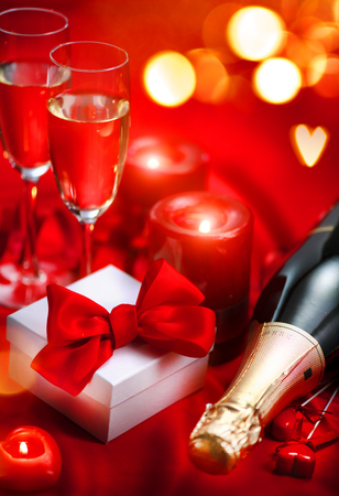 Valentine's Day romantic dinner. Champagne, candles and gift box over holiday red backgroundの写真素材