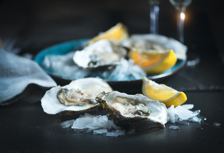 Fresh oysters close-up on blue plate, served table with oysters, lemon and champagne in restaurant. Gourmet foodの素材 [FY31095303463]