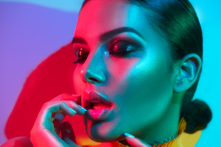 Fashion model woman in colorful bright lights with trendy makeup and manicure posing in studioの写真素材