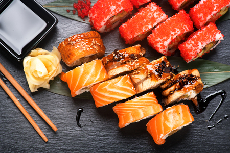 Sushi rolls closeup. Japanese food in restaurant. Roll with salmon, eel, vegetables and flying fish caviar on black slate backgroundの写真素材