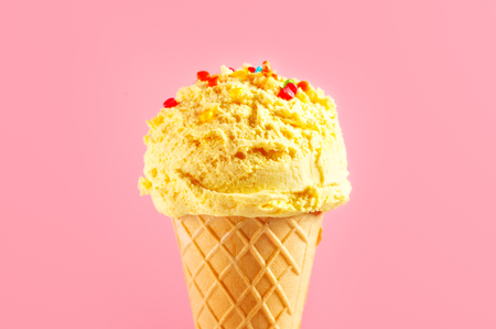Ice cream. Vanilla, banana or lemon flavor icecream in waffle cone over pink background. Sweet dessert decorated with colorful sprinkles closeupの写真素材