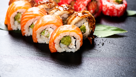 Sushi rolls closeup. Japanese food in restaurant. Roll with salmon, eel, vegetables and flying fish caviar on black slate backgroundの写真素材