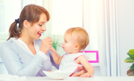 Mother feeding her baby girl with a spoon. Baby food. Healthy familyの写真素材