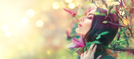 Happy beautiful girl enjoying nature. Blooming magnolia. Beauty young woman touching spring magnolia flowersの写真素材