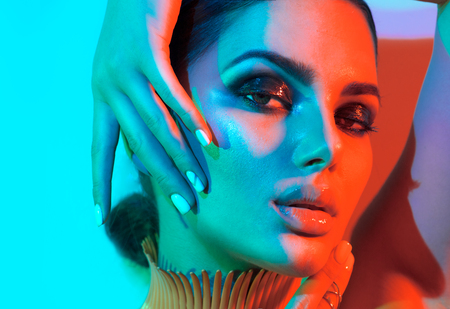Fashion model woman in colorful bright lights with trendy makeup and manicure posing in studioの写真素材