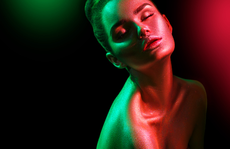 Fashion model woman in colorful bright sparkles and neon lights posing in studio, portrait of beautiful sexy girl. Art design colorful vivid makeupの写真素材