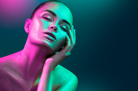 Fashion model woman in colorful bright sparkles and neon lights posing in studio, portrait of beautiful sexy girl. Art design colorful vivid makeupの写真素材