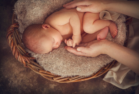 Beautiful newborn baby studio portrait sleeping in a basket over brown background in mother hands. Sweet baby portrait over rustic backgroundの写真素材