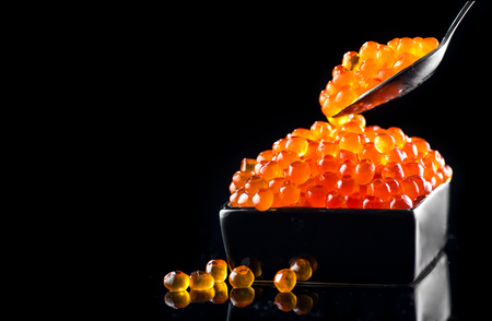 Caviar in a spoon. Salmon caviar in a bowl over black background. Closeup trout caviarの写真素材