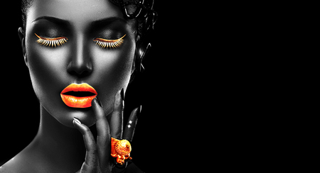 Fashion model with black skin, golden lips, eyelashes and jewellery - golden ring on hand. Isolated on black background. Beauty woman face, beautiful make-up. Gorgeous lady fashion art portraitの写真素材