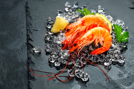 Shrimps. Fresh prawns with lemon on a black background. Seafood on crashed ice, slate tray dark vintage background, top viewの写真素材