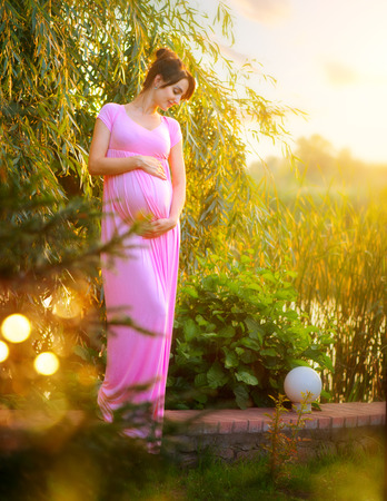Pregnant happy woman caressing her belly in summer park. Full length pregnant beauty woman outdoor portrait. Healthy pregnancy conceptの写真素材